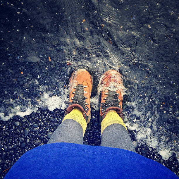 Hiking boots on a shore of stones with water washing over, from a personal perspective.  Photo captured with an iPhone.
