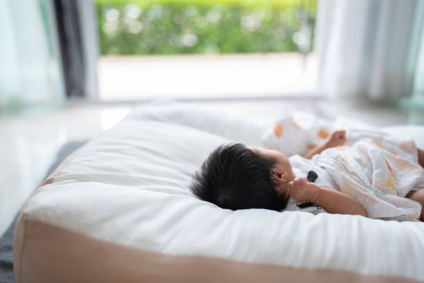 Asian baby girl lying down on back on the bed and looking at view stock photo