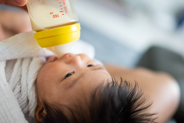 Hand of a mother holding milk bottle and feeding her newborn baby while the baby looking at her with love. stock photo