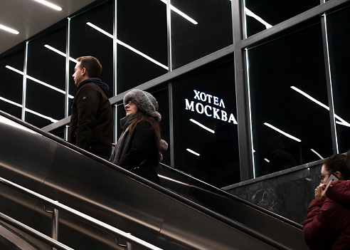 Belgrade, Serbia- November 20, 2023: People going up the subway escalator, with interior lights reflecting and hotel Moskva sign in the night