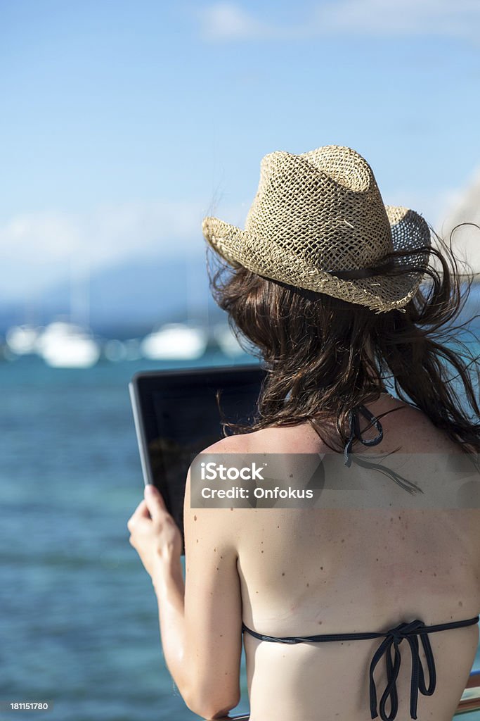 Woman Using an Electronic Tablet on Over Water Bungalow Balcony Woman Using an Electronic Tablet on Over Water Bungalow Balcony. The woman is sitting on a chair and relaxing at paradise tropical resort on a nice day. Adult Stock Photo