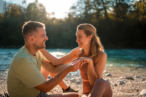 A Caucasian couple shares a moment as the man proposess by the river.