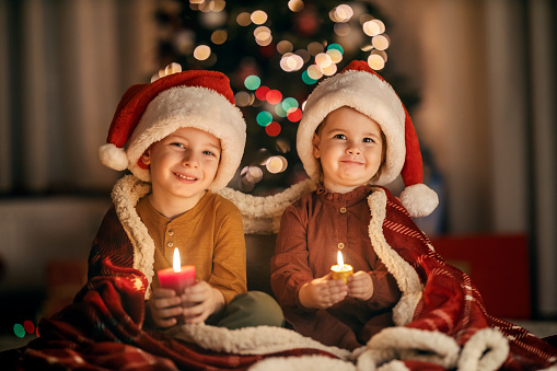 Jolly adorable brother and sister holding candles on christmas eve and smiling at the camera. Christmas joy and magic.