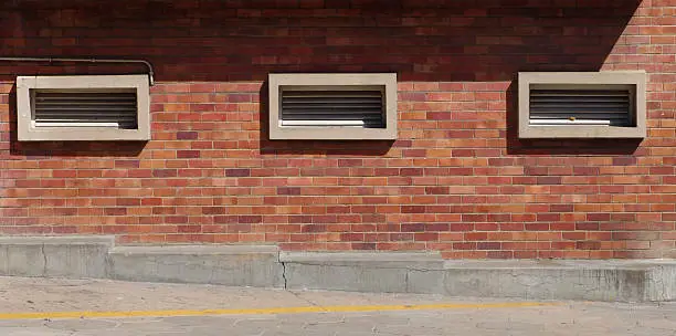 A brick wall with airvents along a sidewalk.