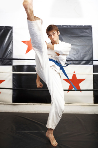 Karate trainer practicing a roundhouse kick in a boxing ring - full length