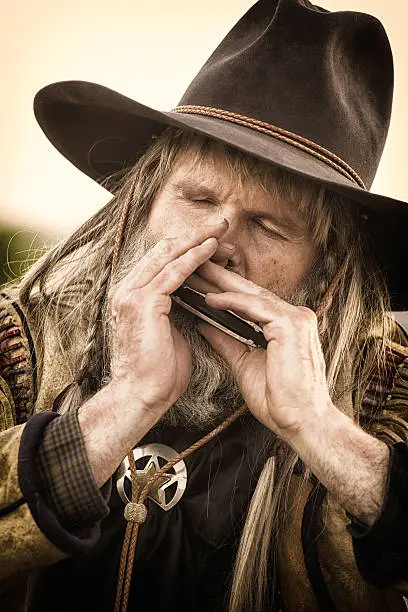 Close-up of an old cowboy playing the harmonica with all his soul.