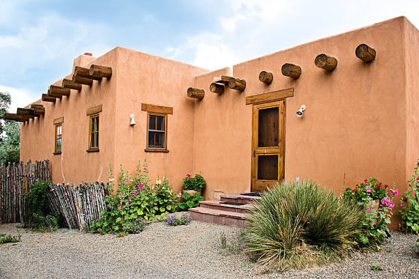Santa Fe Old Adobe House with Stucco Wall and Flowers Sant Fe Pueblo-style homes are built with bricks of tightly compacted earth, clay and straw. These houses borrow architectural details from the adobe homes of early Native Americans and feature massive walls, flat roofs, heavy timbers extending through the walls to support the roof, deep window and door openings and simple windows. adobe material stock pictures, royalty-free photos & images