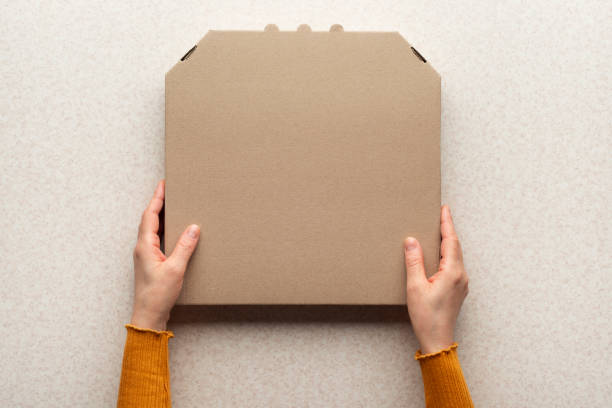 istock Pizza closed carton box in caucasian hands on kitchen table flat lay mockup with copy space 1811590945