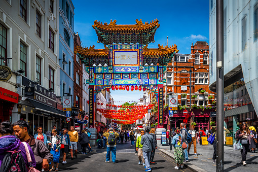 London, United Kingdom - May 29, 2023:  Crowded street with entrance gate to in Cinatown in London.