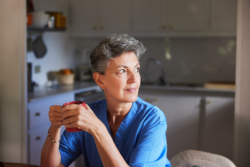 Reflective Moment: Nurse in Blue Scrubs Takes Pause with Coffee Mug