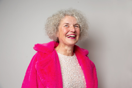 Senior woman wearing pink fur coat and glittery dress, laughing