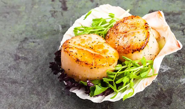 Pan seared scallops with garnish on a stone plate..