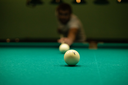 A man plays billiards and prepares to hit. A man aims his cue at a billiard ball while leaning towards the table. In the evening, a man relaxes after work by playing billiards.