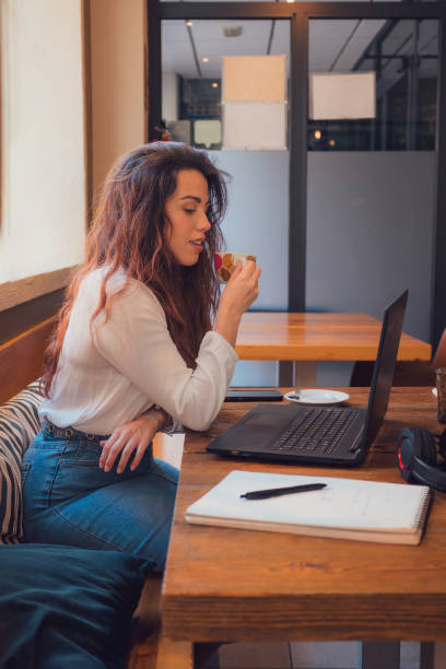 istock Young adult woman working with a laptop from a restaurant while drinking coffee 1811659383