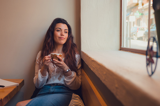 Relaxed woman drinking coffee in a restaurant while she is looking out the window