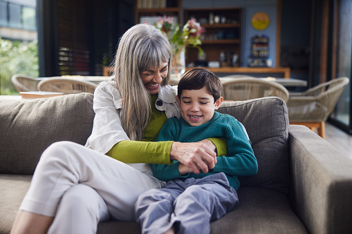 Smiling grandmother and her adorable little grandson talking while sitting together on a living room sofa during a visit