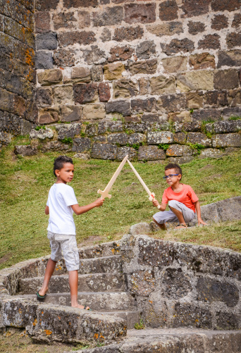Brothers playing with wooden swords next to a medieval castle in France