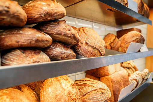 Variety of fresh artisan breads with crispy crusts displayed on metal shelves in a bakery.