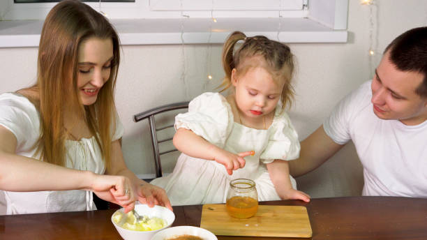 a little girl enjoys some honey from a jar - two parent family indoors home interior domestic kitchen imagens e fotografias de stock