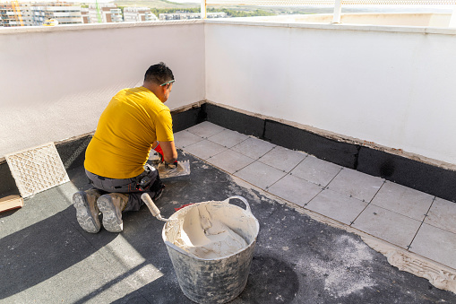 Latino worker kneeling on the floor laying terrace tiles.