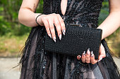 Close-up of a woman wearing a formal black dress, her hands with an attractive manicure, holding a glittering handbag. Selective focus.