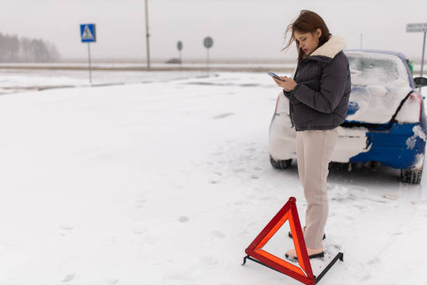 młoda kobieta, która rozbiła swój samochód na śliskiej zimowej drodze w śniegu, dzwoni po lawetę z trójkątem awaryjnym obok niej w pobliżu samochodu. - car winter road reflector snow zdjęcia i obrazy z banku zdjęć