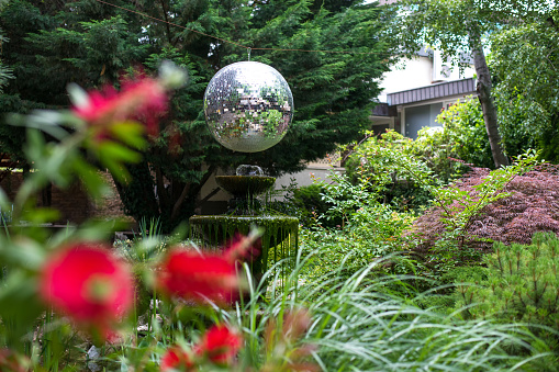 Garden exterior with fountain, trees, bushes, flowers and attractive shiny ball. Selective focus.