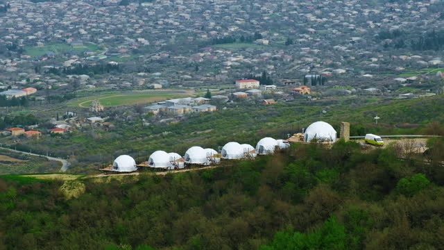 Spherical houses on a green hill. Glamping area with white eco dome tents