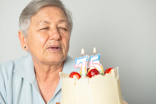 Senior women with birthday cake on white background.