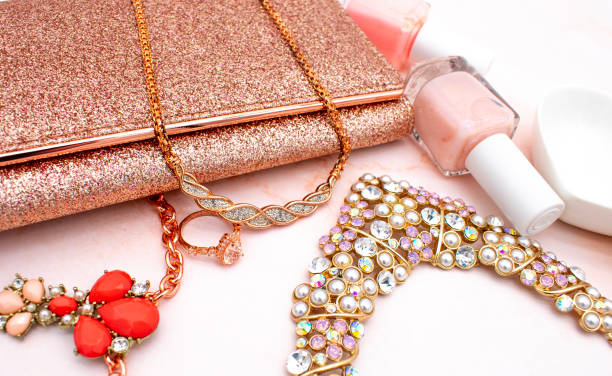 ローズクォーツの背景、ピンクのマニキュア、キラキラのクラッチ財布、ローズゴールドのダイヤモンドジュエリーとローズゴールドのフラットレイファッションとジュエリーのコンセプト