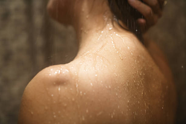 femme prenant une douche, avec un accent sur son dos et ses épaules. gros plan sur sa peau et ses gouttes d’eau. - femme douche photos et images de collection