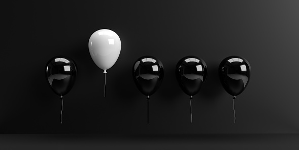 Leadership and teamwork concept. A single white balloon stands out from the rest black balloons as a symbol of leadership. 3D rendered objects with large copy space.