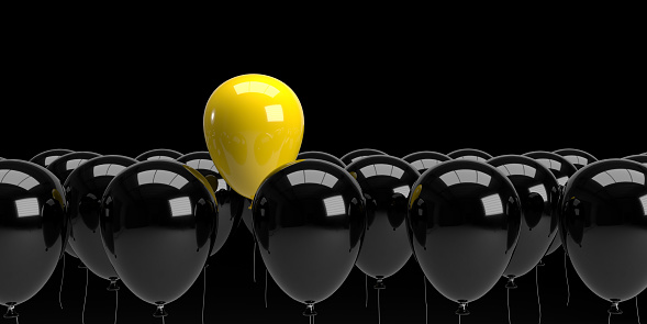 Leadership and teamwork concept. A single yellow balloon stands out from the rest black balloons as a symbol of leadership. 3D rendered objects with large copy space.