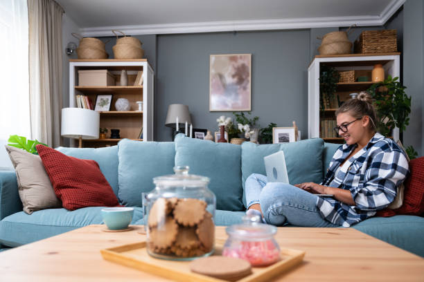 istock Young female freelancer in casual clothes sitting on comfortable couch and working remotely on laptop. Woman copyright writer or web developer work at home sitting on sofa enjoying her freedom. 1811765463