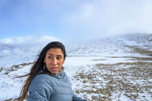 middle-aged latina woman on a snow-capped mountain in a blizzard,
