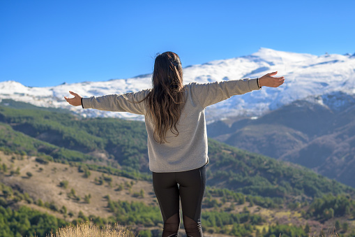 Hiker on her back with arms outstretched happily enjoying the scenery while walking outdoors in winter,