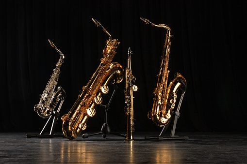 Four different saxophones  on stands. Golden, silver and straight saxophones on the black floor of concert stage. Shallow depth of field.