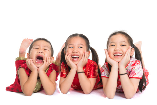Group of happy young Asian children in traditional Cheongsam dress lying on floor with head on hands, isolated on white background