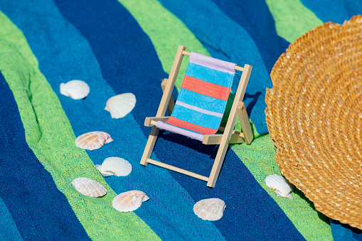 Little wooden armchair and shells with hat on towel on beack
