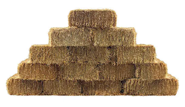 Bale of hay group in a pyramid wall pattern isolated on a white background as a country living design element and agriculture farm and farming symbol of harvest time with dried grass straw as bundled tied haystacks.