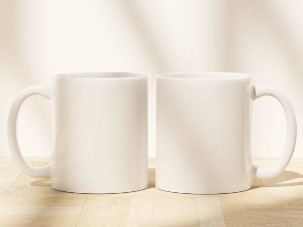 istock Two white coffee cups on a wooden floor with soft shadows from window pane 1811913668