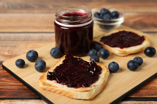 Delicious toasts with blueberry jam and fresh berries on wooden table