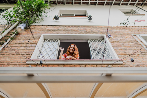 Portrait of mid adult woman waving at the camera through the hostel window