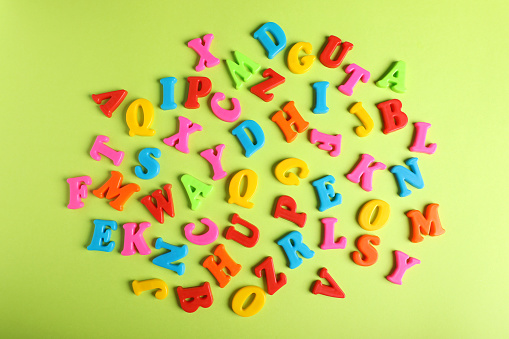 Many colorful magnetic letters on light green background, flat lay