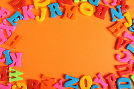 Frame made of many colorful magnetic letters on orange background, flat lay. Space for text