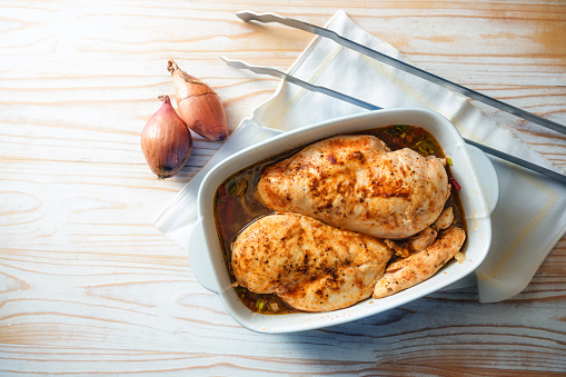Meat dish from spicy chicken breast fillet with onions and vegetable broth in a casserole for the oven, cooking poultry at home, high angle view from above, copy space, selected focus