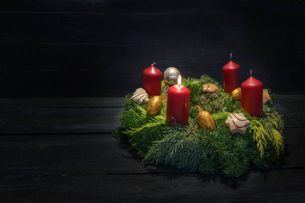 istock Light in the dark on first advent, natural green wreath with red candles, one is burning, Christmas decoration and cookies, dark wooden background, copy space 1812054026