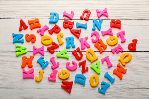 Colorful magnetic letters on white wooden table, flat lay