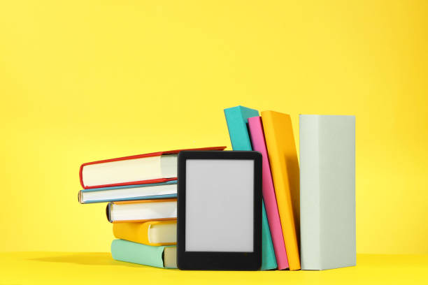istock Modern e-book reader and hard cover books on yellow background 1812058898