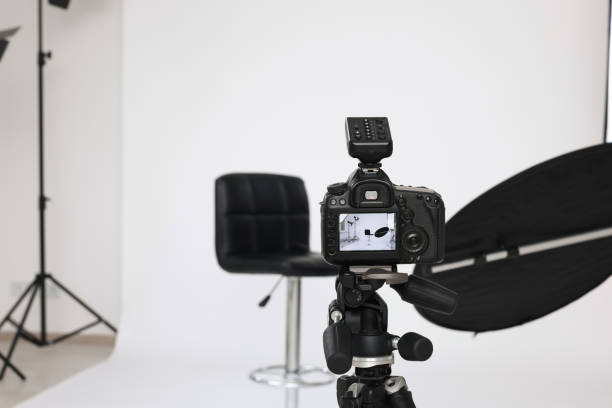 istock Camera on tripod, bar stool and professional lighting equipment in modern photo studio, space for text 1812072842